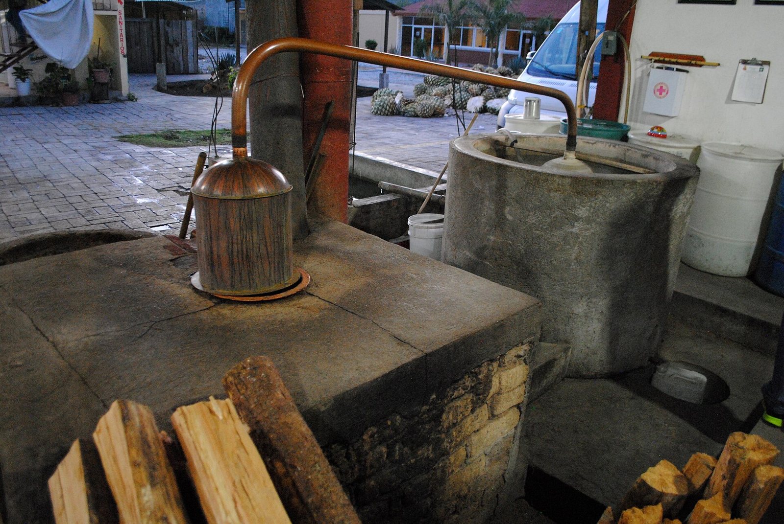 Copper still on a stone furnace next to a cooling tank and firewood