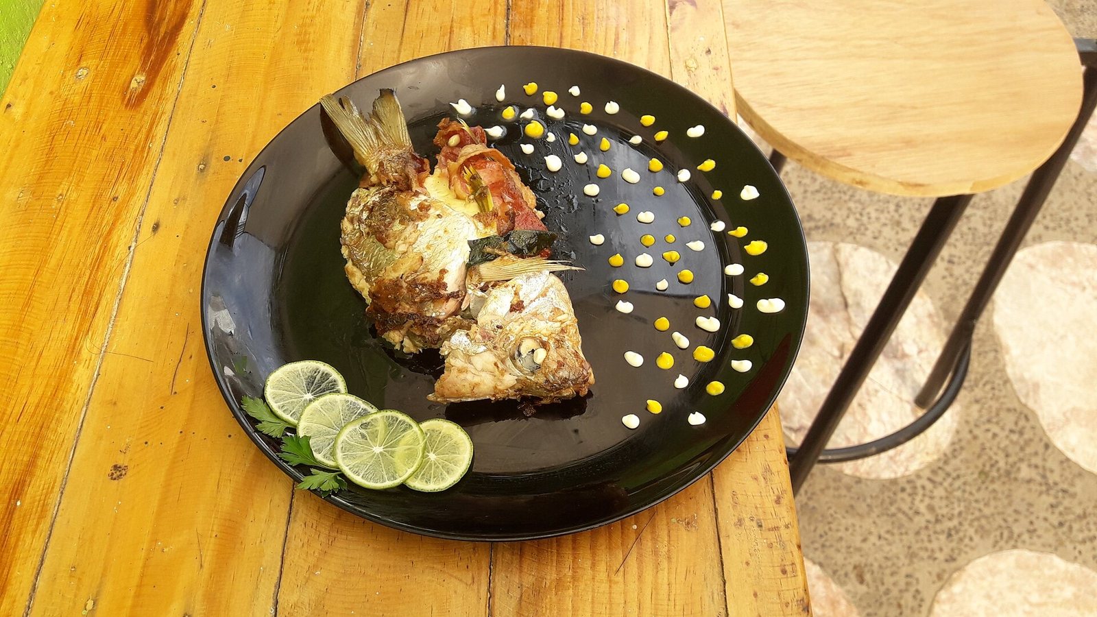 Butterflied pescado zarandeado on a black plate with limes, on a wooden counter