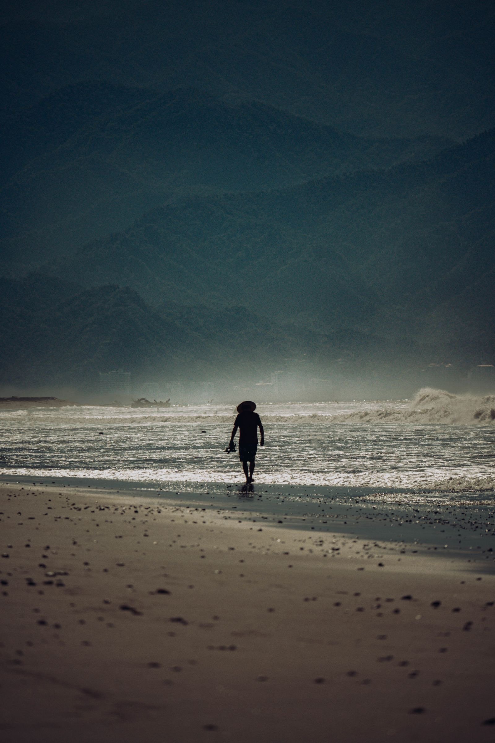Person walking alone along the shoreline in Nuevo Vallarta with misty mountains behind