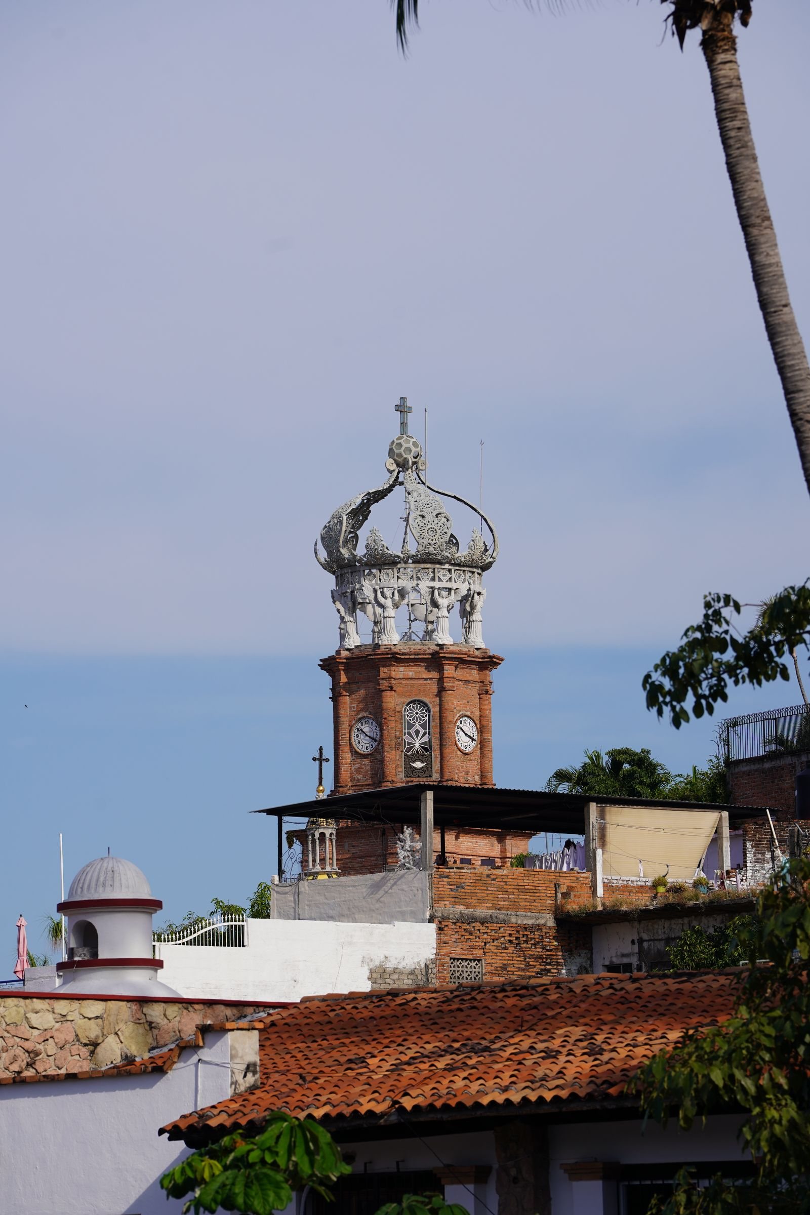 Brick clock tower topped by the white crown of Puerto Vallarta's parish church, above tiled rooftops