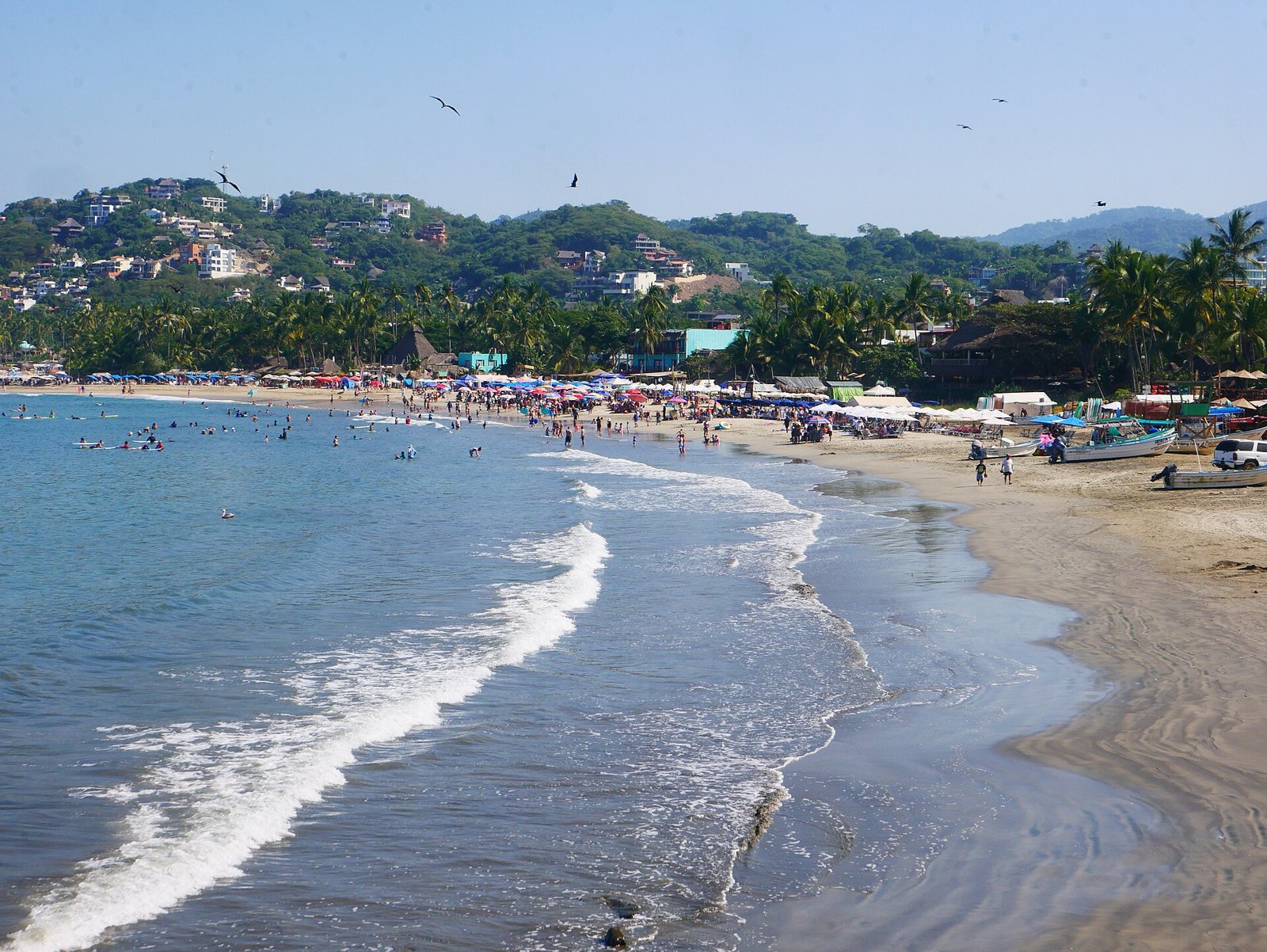 Whitewater rolling onto the shore of Sayulita main beach, with people in the water and palapas behind
