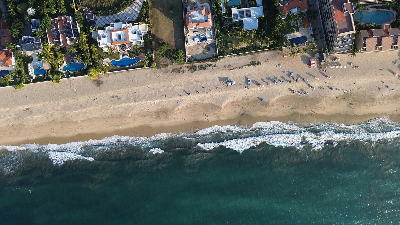 Aerial view of waves breaking on the wide sand of San Pancho beach, with houses behind