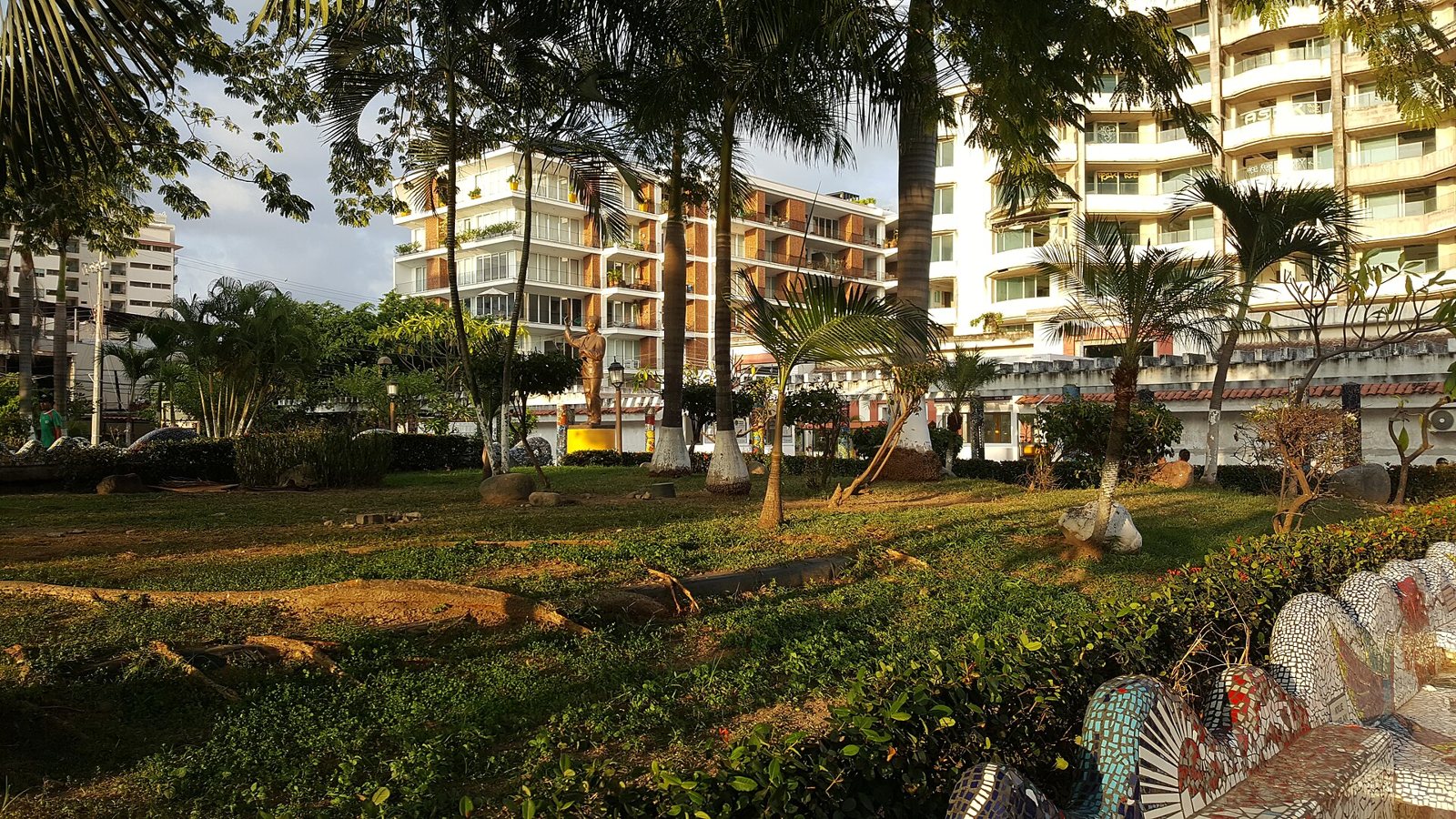Lázaro Cárdenas Park with palm trees, a gold statue of the former president and mosaic benches in the foreground
