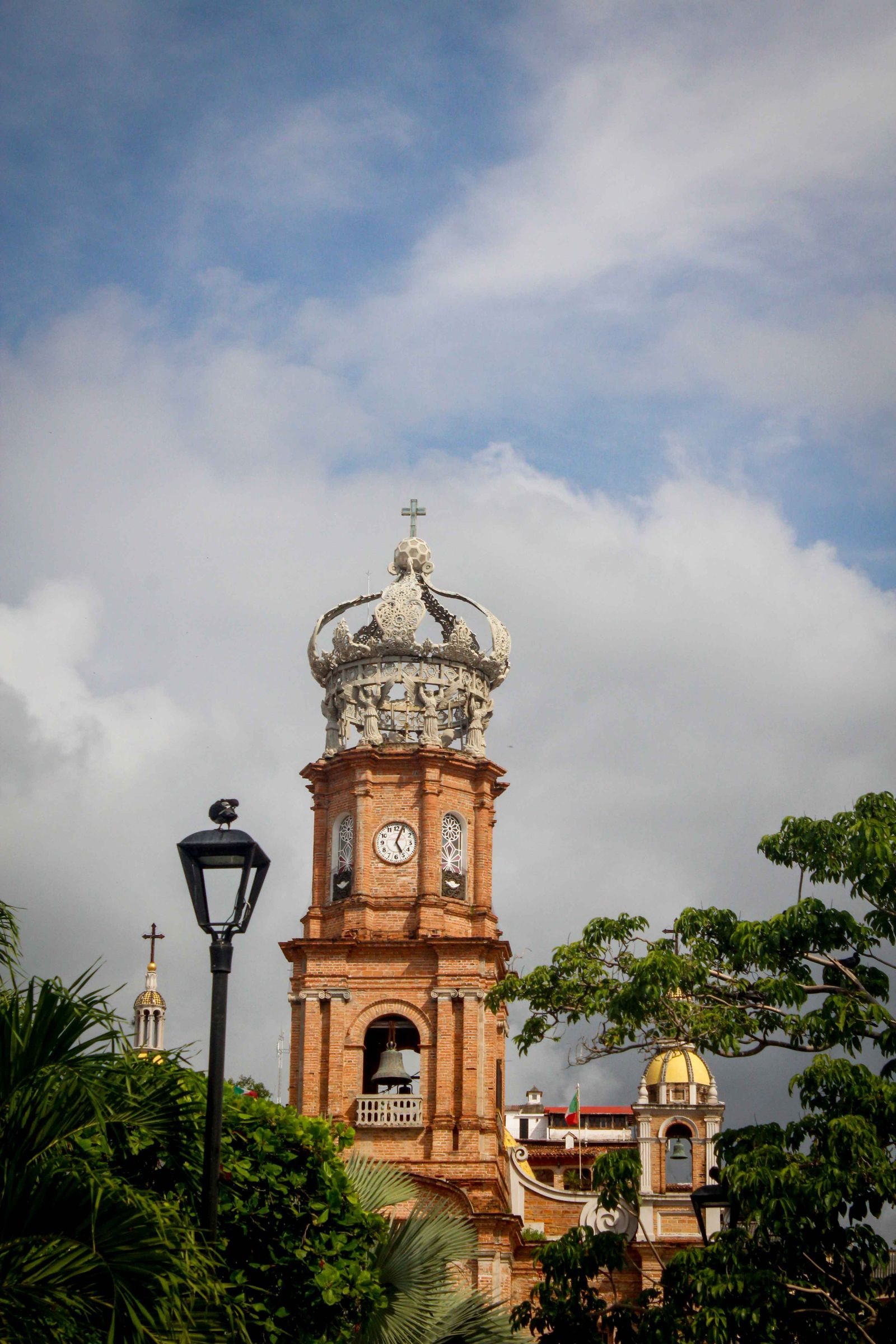 Brick bell tower with a clock and white crown of the Our Lady of Guadalupe church in Puerto Vallarta