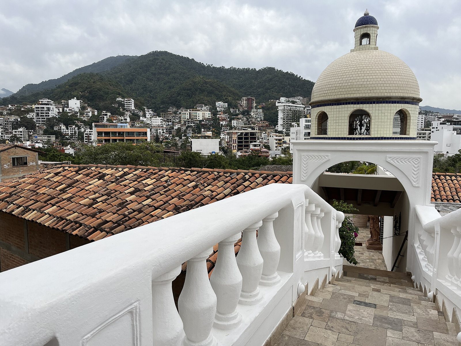View from the Casa Kimberly bridge with a white balustrade, a tiled dome and Puerto Vallarta's green hills behind