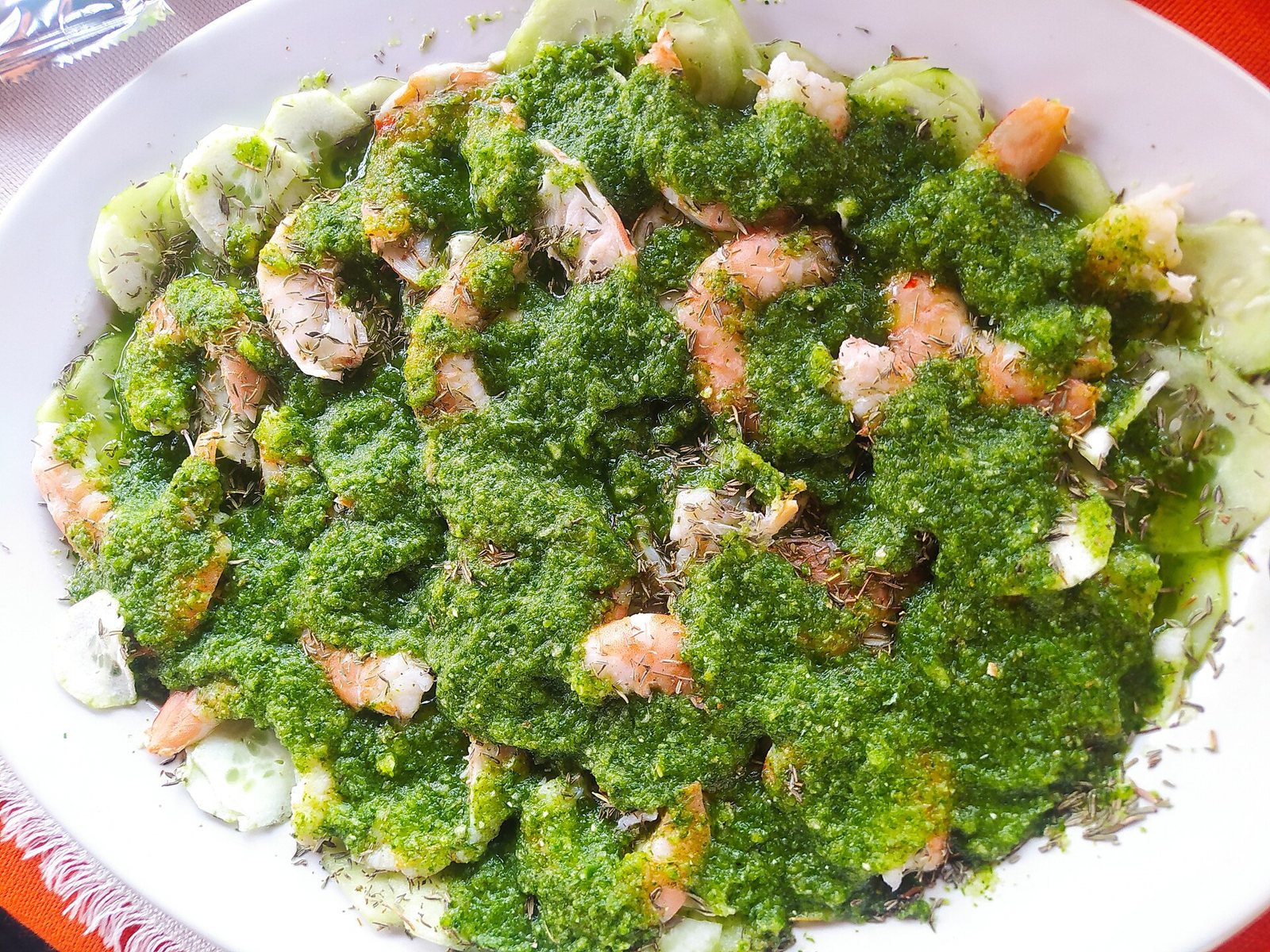 Plate of green aguachile with raw shrimp covered in green chile sauce over cucumber slices
