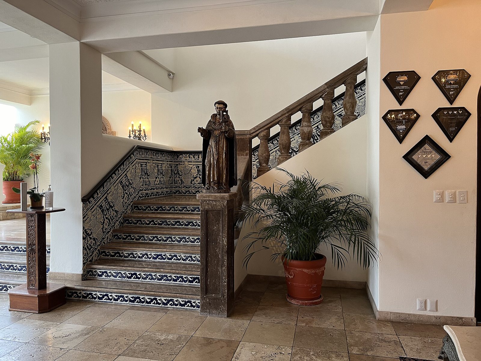Blue-and-white tiled staircase with a stone balustrade and a carved wooden religious statue in the lobby of Casa Kimberly