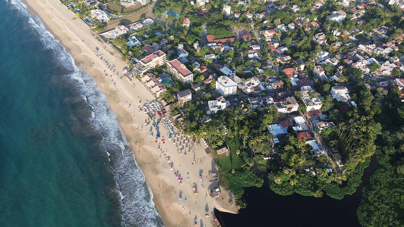 Aerial view of the beach at San Francisco (San Pancho), Nayarit, with colorful umbrellas, palm trees, the town and an estuary by the sea