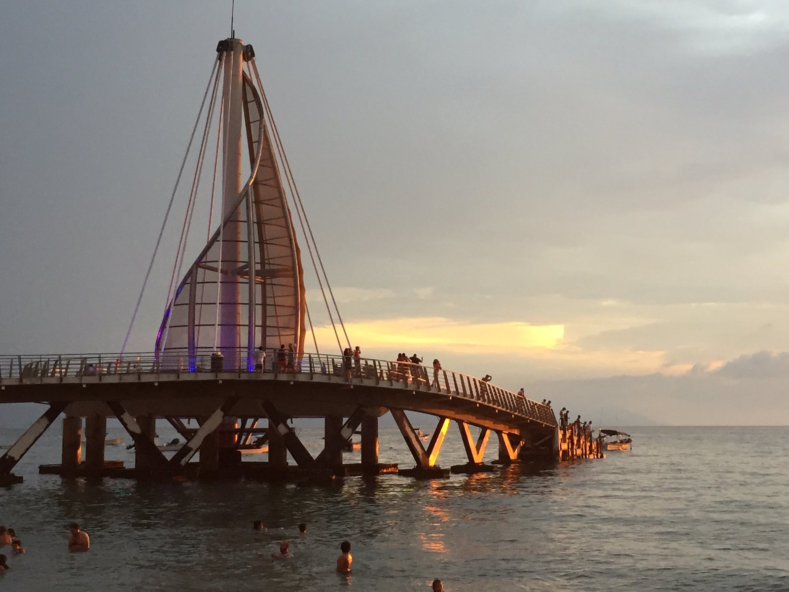 Los Muertos Pier with its sail-shaped structure lit up at sunset and people walking along it