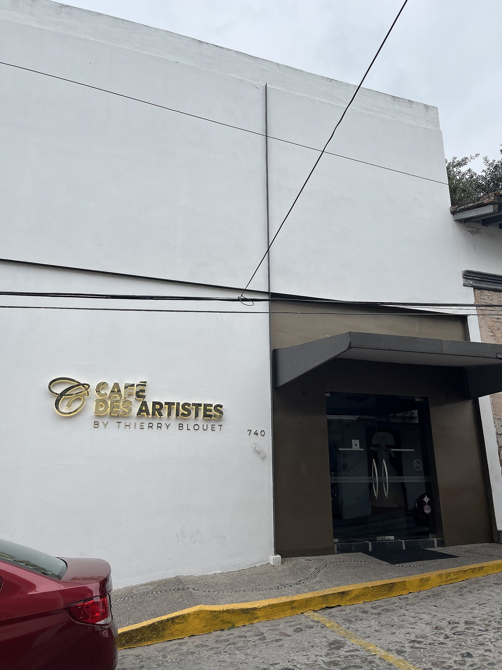White facade of Café des Artistes by Thierry Blouet with gold lettering and the street number 740 on a cobblestone street downtown