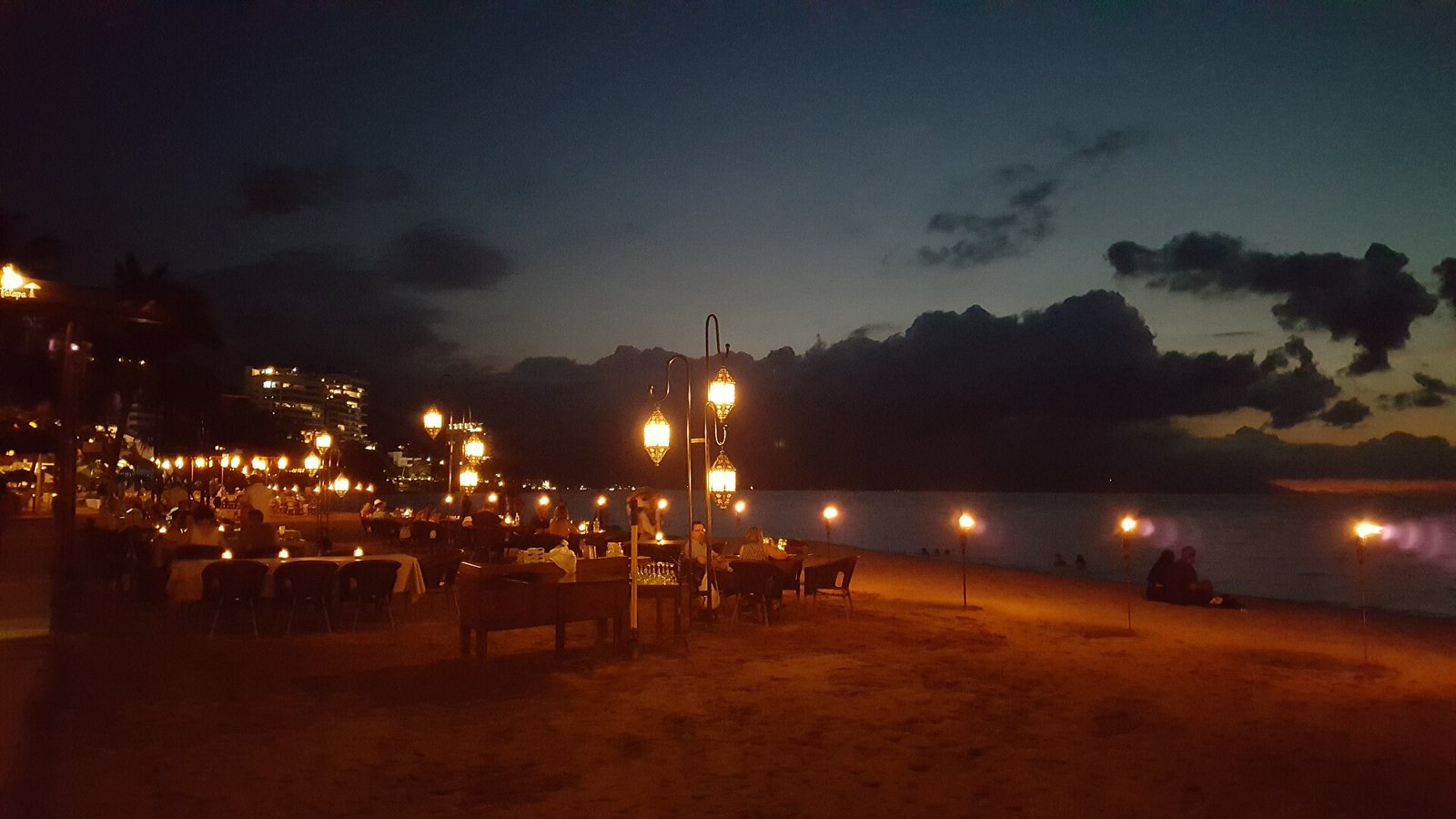 Tables lit by lanterns and torches on the sand by the ocean after dark on Los Muertos Beach