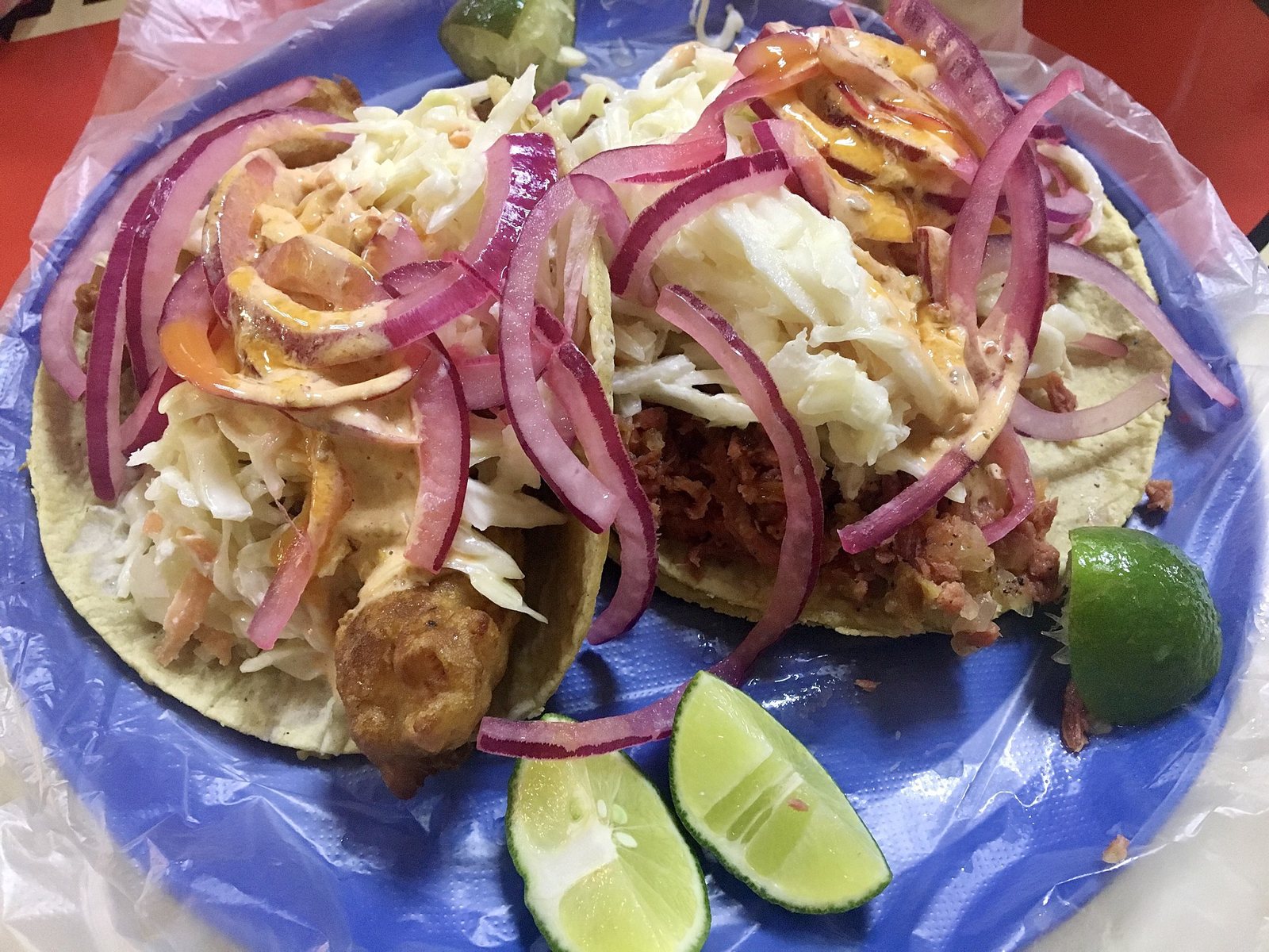 Two battered fish tacos topped with cabbage slaw, pickled red onion and creamy sauce, served with lime wedges