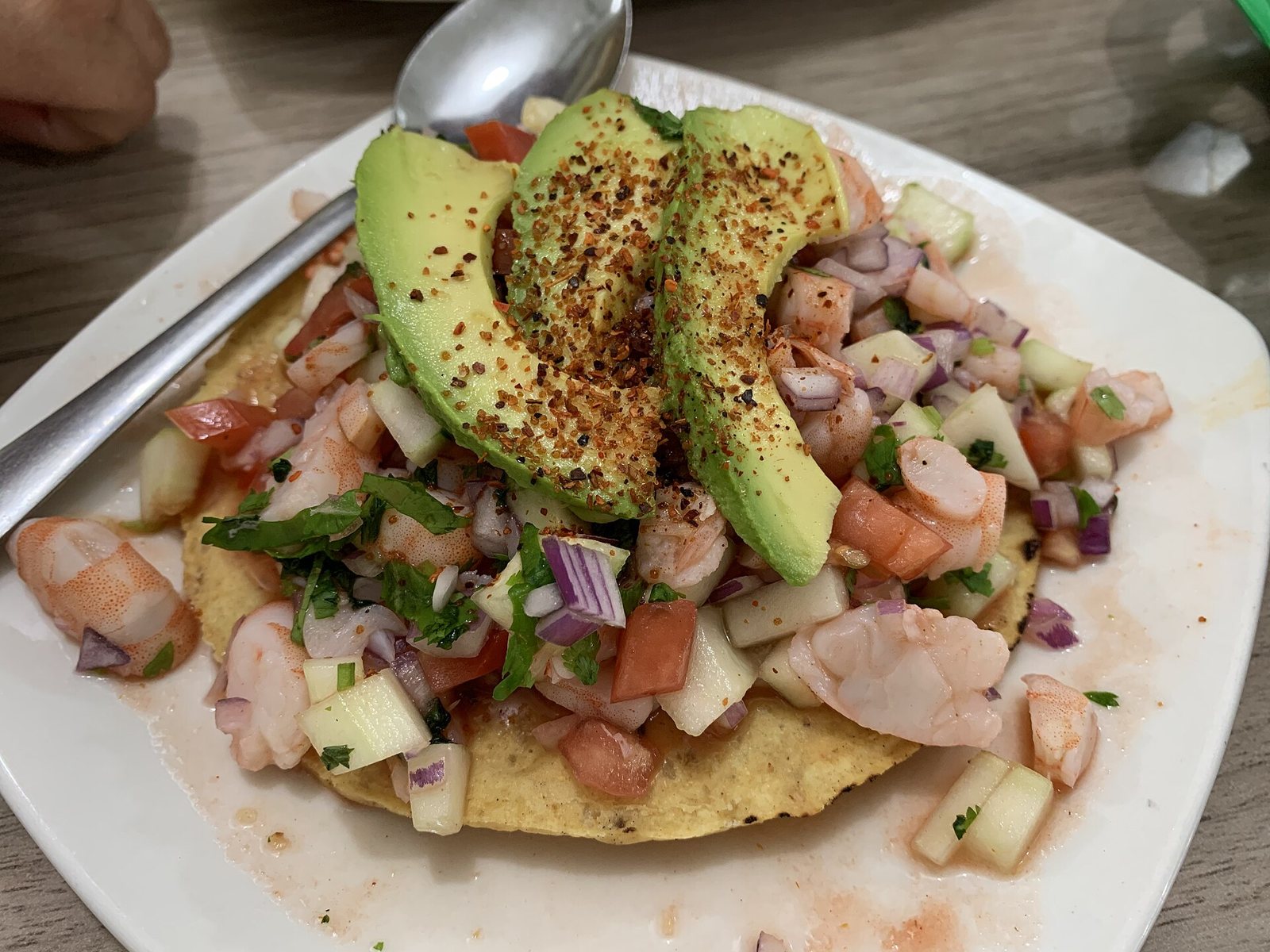 Shrimp ceviche tostada with tomato, cucumber, red onion, cilantro and avocado slices dusted with chili powder