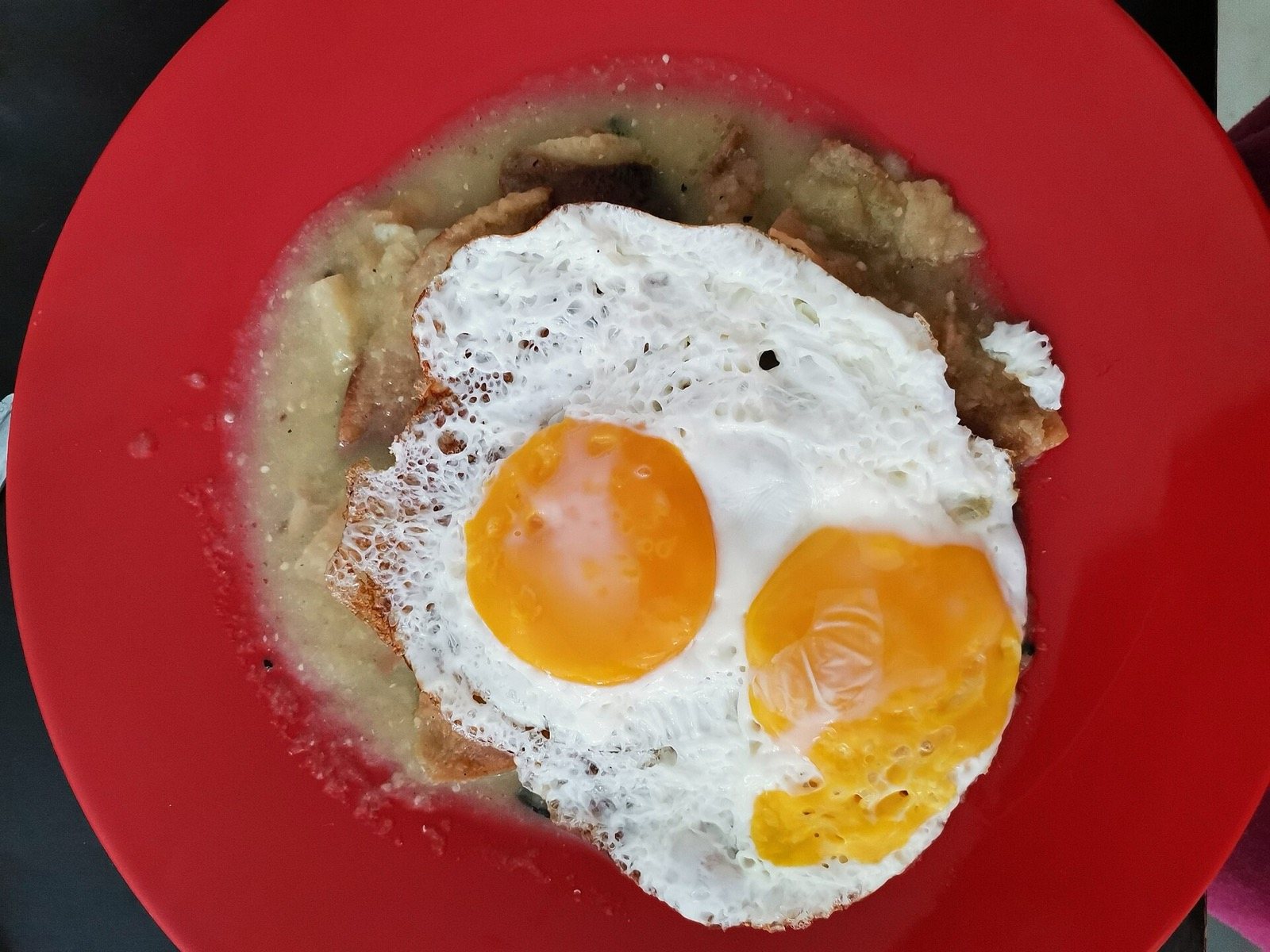Red plate of chilaquiles in green salsa topped with two sunny-side-up eggs