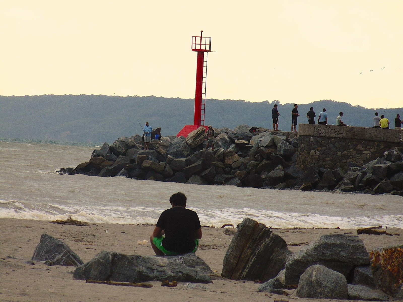 Red lighthouse on the Nuevo Vallarta marina jetty, with people fishing and mountains behind