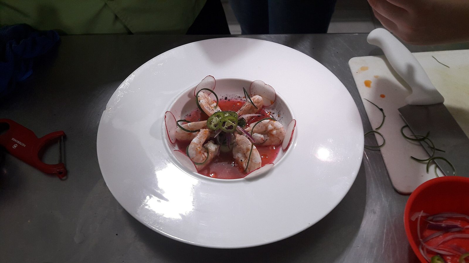 White bowl of raw shrimp in a red chili and lime broth, garnished with radish slices and a ring of chile