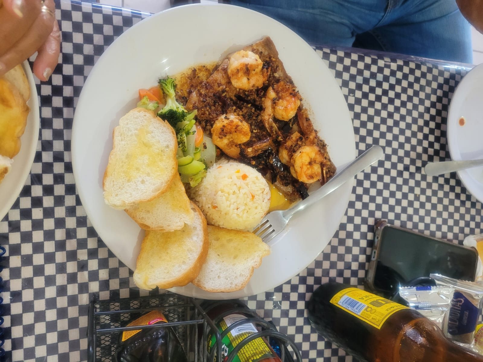 Plate of garlic-chili shrimp with rice, vegetables and toasted bread on a checkered tablecloth