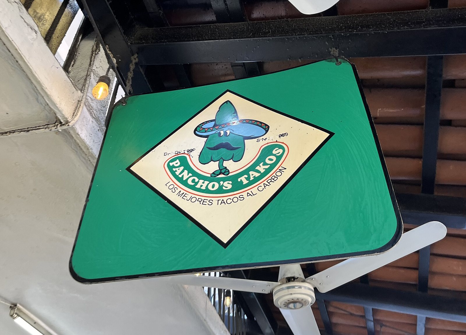 Green hanging sign for Pancho's Takos reading "Los mejores tacos al carbón" under a tiled roof
