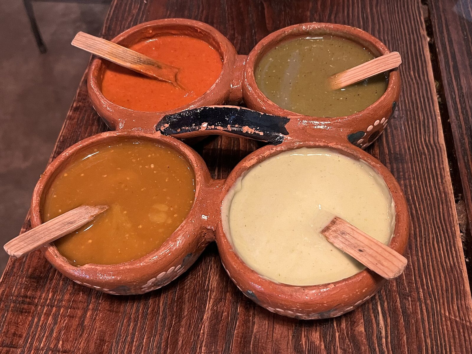 Clay salsa holder with four salsas in red, green, orange and cream, each with a small wooden spoon