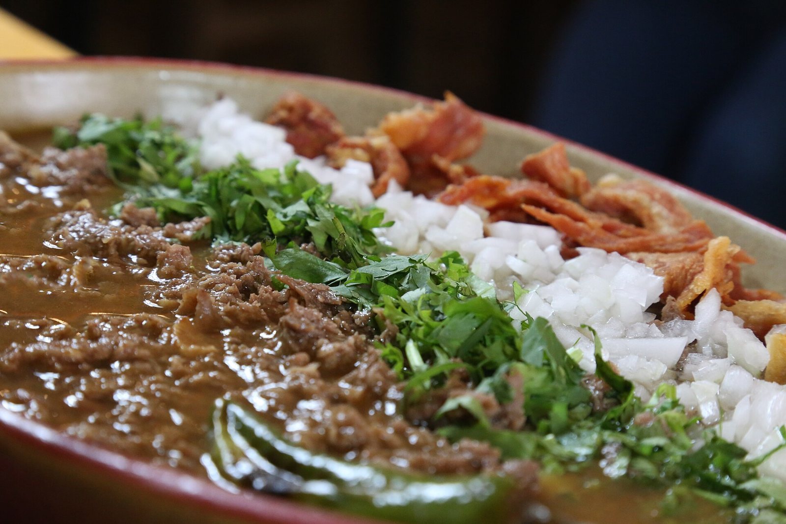 Clay dish of carne en su jugo with minced beef in broth, cilantro, chopped onion and crispy bacon