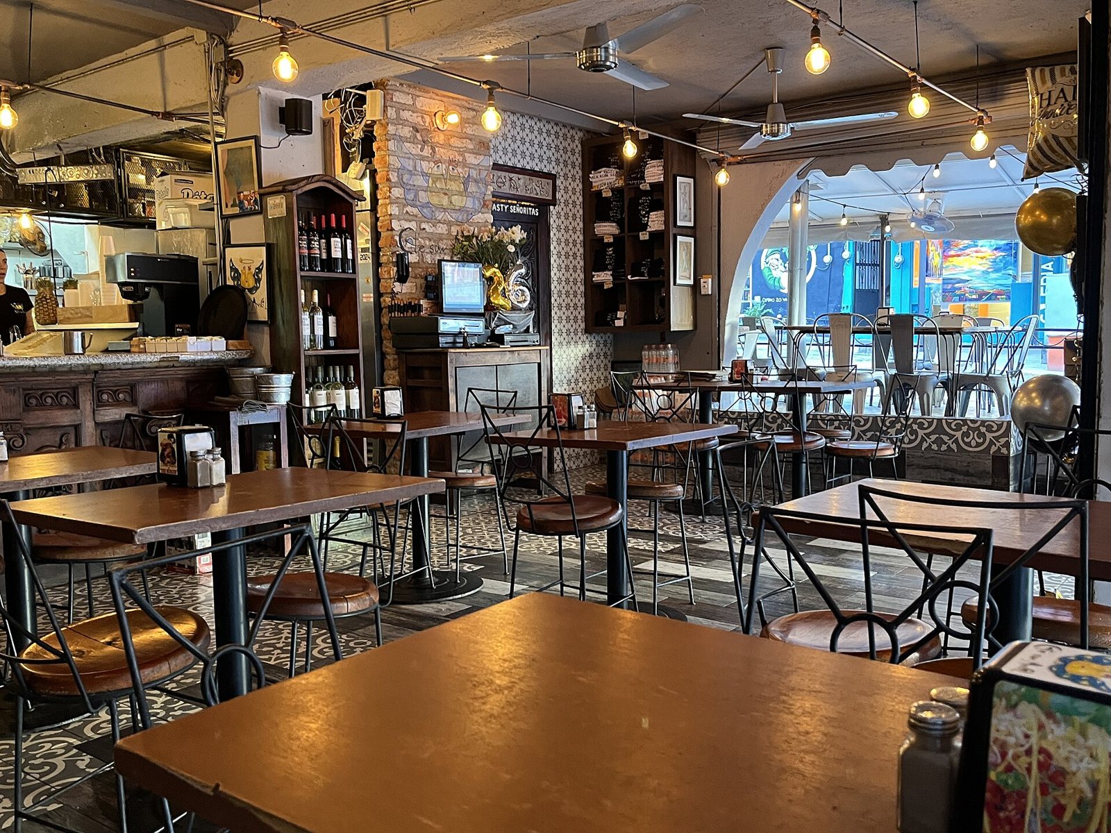 Inside Café San Ángel, with wooden tables, wrought-iron chairs, patterned tile floor, hanging string lights and a coffee bar