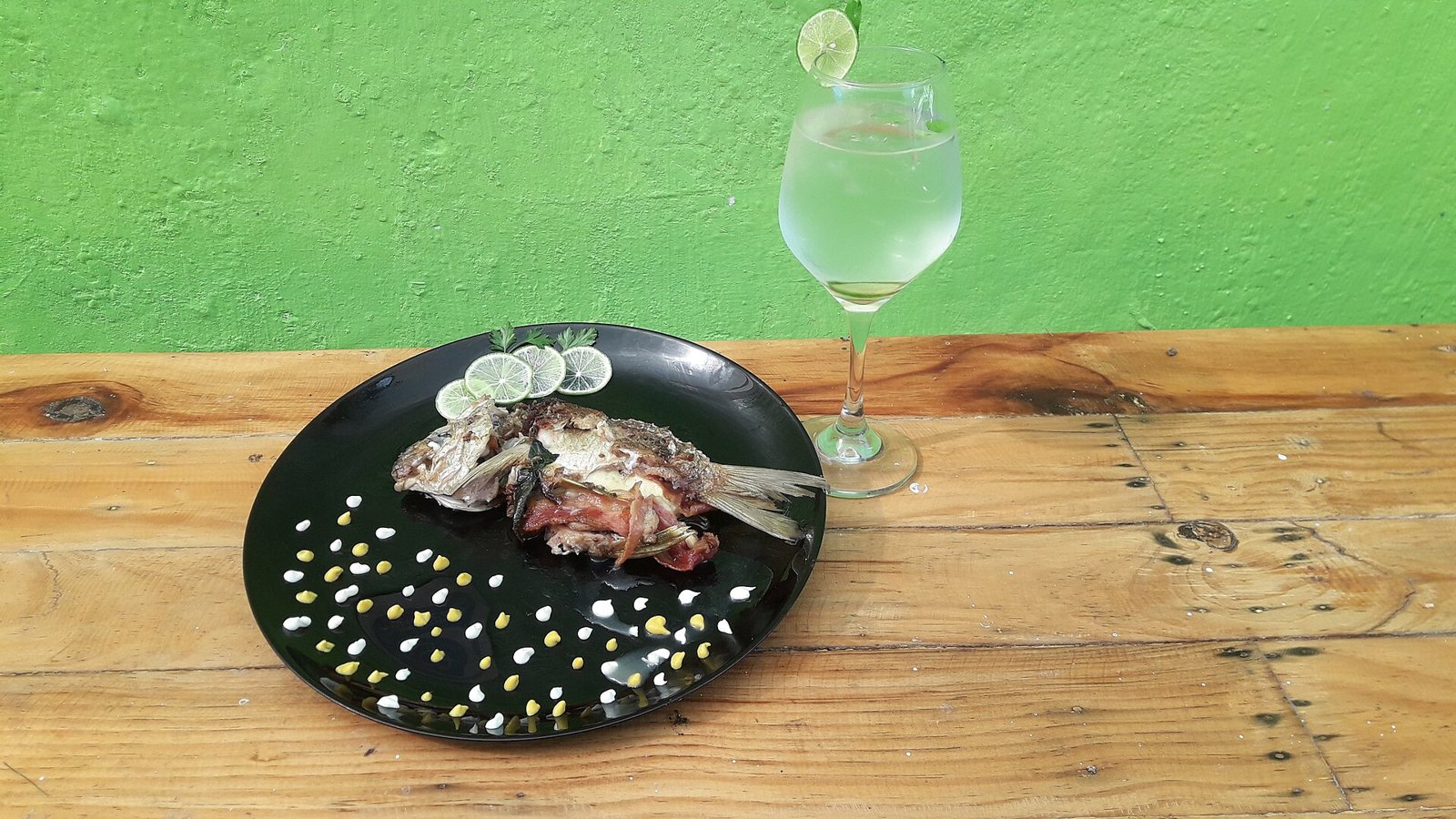 Whole grilled fish served on a black plate with lime slices, next to a glass of water